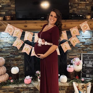 Robe de maternité bordeaux avec ceinture florale dans un décor de fête