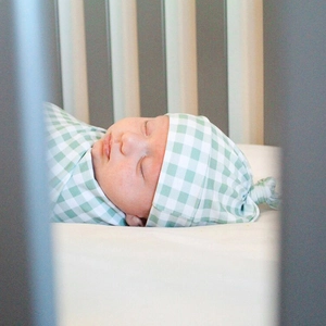 Green gingham baby swaddle wrap and matching knotted hat set for newborns sleeping in crib