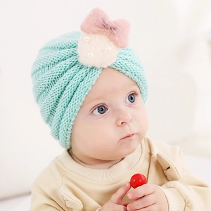 Détail du bonnet tricoté bébé vert menthe avec nœud en velours rose et pompon perlé