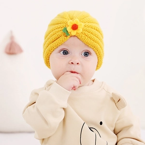 Detail of yellow knit baby turban hat with handmade crochet sunflower and green leaves