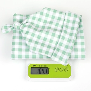 Weight measurement of green plaid baby swaddle and knotted hat set on a digital scale