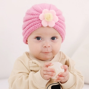 Détail d'un bonnet turban en tricot rose pour bébé avec fleur en peluche décorative