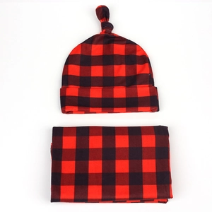 Flat lay of buffalo plaid newborn swaddle blanket and knotted hat set in red and black