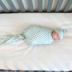 Green plaid baby swaddle set with matching knotted hat on white bedding background