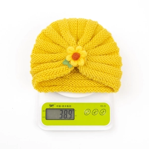Detail view of yellow knit baby hat with crochet flower showing weight of 38.9g on scale