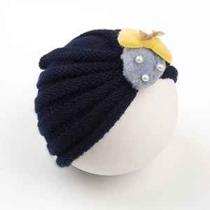 Détail d'un bonnet tricoté bleu marine avec fourrure, feuilles en feutre et perles