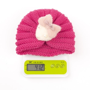 Détail d'un bonnet en tricot rose pour bébé avec nœud pesé à 41,2g sur une balance numérique