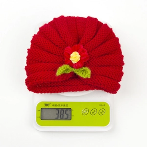 Lightweight red knit baby hat with crochet flower detail on a digital scale weighing 38.5g