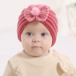 Detail of pink knit infant turban hat featuring a large bow and soft plush pompom