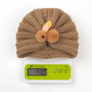 Close-up showing the weight of light brown baby knit hat with cute plush rabbit on scales