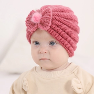 Detailed knit texture of dark pink infant beanie featuring a soft bow and faux fur pompom