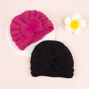 Detailed texture of knitted baby beanies with bows and soft pompom embellishments