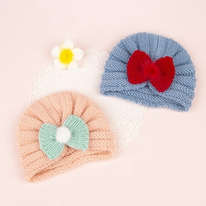 Detailed knit texture of infant beanies with colorful bows and decorative pom-poms