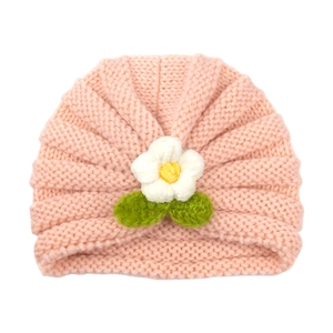 Pink knit baby turban hat featuring a decorative white crochet flower and green leaves