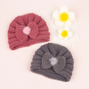 Close-up of baby knitted beanies featuring a textured bow and faux fur pom-poms