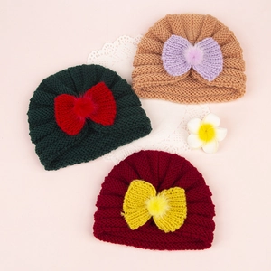 Detailed view of three knitted baby hats with large bows and pom-poms on pink background