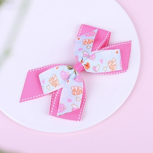 Close-up of pink and blue layered bow hair clip with heart patterns on a white tray