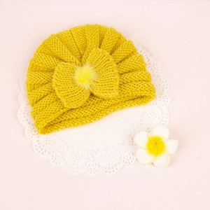 Close-up of yellow knit baby turban hat with bow and pompom on pink background