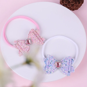 Detail of two nylon baby headbands with sequin bows and heart rhinestones on a white tray