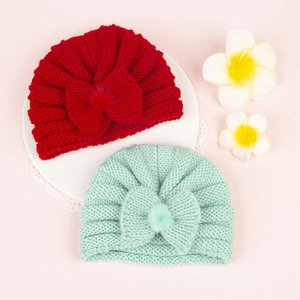 Detail of red and mint green baby knit hats with large bows and plush pompoms