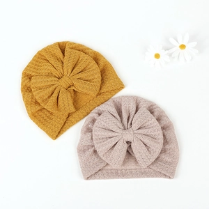 Detail view of waffle knit baby turban hats with large bows in yellow and pink colors