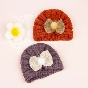 Flat lay of warm knit baby turban hats with bows and pom-poms in ginger and purple