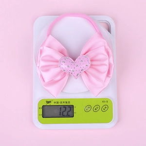 Pink bow baby headband showing lightweight 12.2g mass on scale for comfort