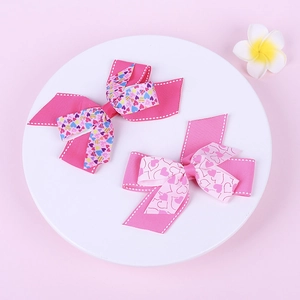 Close-up of pink ribbon hair clips with gold heart patterns and white stitched edges