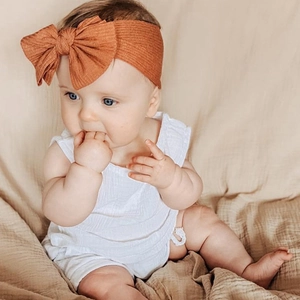 Detail of baby ribbed cotton headband with large bow in caramel brown on a warm background