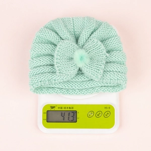 Detailed knit texture of light green baby beanie with large bow and faux fur pompom