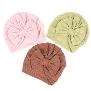 Detailed view of three waffle knit baby beanies in pink, mint, and caramel with large bows