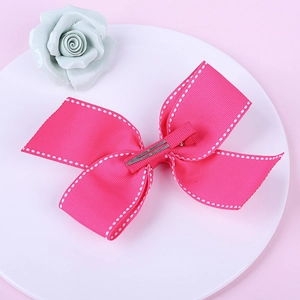Detail showing hot pink grosgrain ribbon bow with white stitching and silver duckbill clip