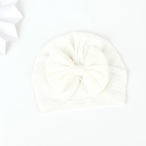 Close-up of a white baby turban hat with a large bow and soft waffle knit texture