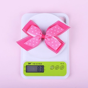 Close-up showing the weight of a pink heart pattern bow hair clip on a digital scale