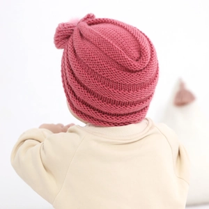 Deep pink chunky knit infant hat with bow decoration shown on baby for warmth
