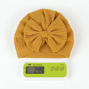 Detail showing ginger yellow waffle knit baby turban hat weighing 24.4g on a digital scale