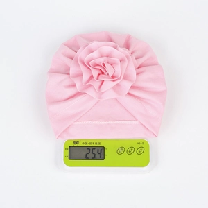 Dettaglio che mostra il peso leggero di 25g del turbante neonato con fiori rosa su scala