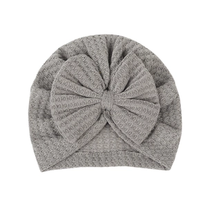 Neutral grey waffle knit baby turban hat with a large bow detail on a plain background