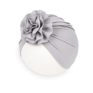 Dettaglio di un turbante grigio per neonati con un grande fiore a pieghe su sfondo bianco