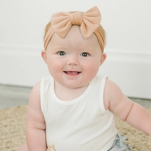 Baby bow headband made of ribbed cotton fabric in beige, worn by a cute toddler model