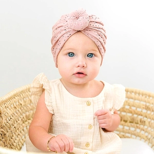 Detailed view of pink knitted baby turban hat with hollow lace pattern and top knot