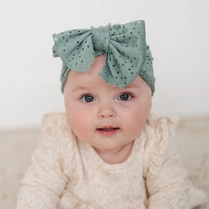 Gros plan d'un bandeau en maille verte avec texture ajourée et grand nœud pour bébé