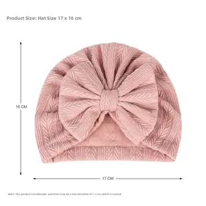 Détail du bonnet tricoté rose clair pour bébé avec grand nœud et dimensions 17x16cm