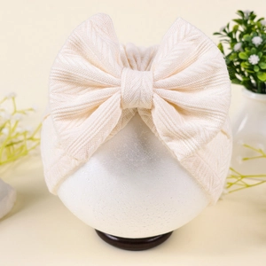 Détail d'un bonnet turban crème pour bébé avec un grand nœud en tricot texturé et doux
