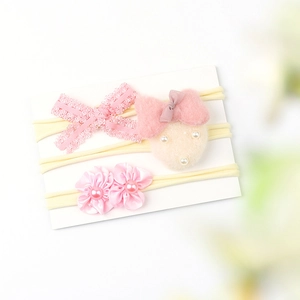 Detail of three pink baby headbands featuring lace bows, plush motifs, and satin flowers