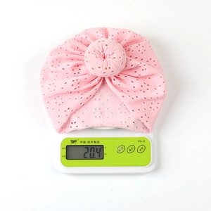 Macro shot of a lightweight 20.4g pink eyelet lace baby turban hat on a digital scale