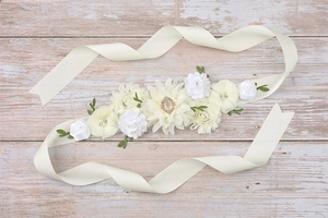 Detail of maternity sash with satin flowers, pearls, and rhinestones on wooden background