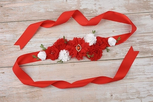 Detail of red maternity flower sash with silk roses and gemstone on wooden background