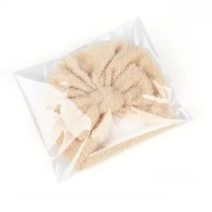 Détail du bonnet pour bébé en polaire beige avec nœud papillon sous emballage neutre