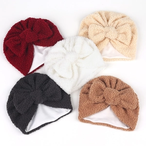 Cinq bonnets en polaire pour bébé avec grands nœuds de différentes couleurs sur fond blanc
